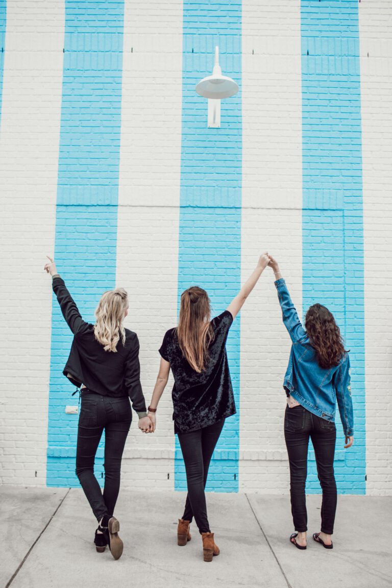 שלוש נשים מרימות ידיים על רקע קיר כחול ולבן